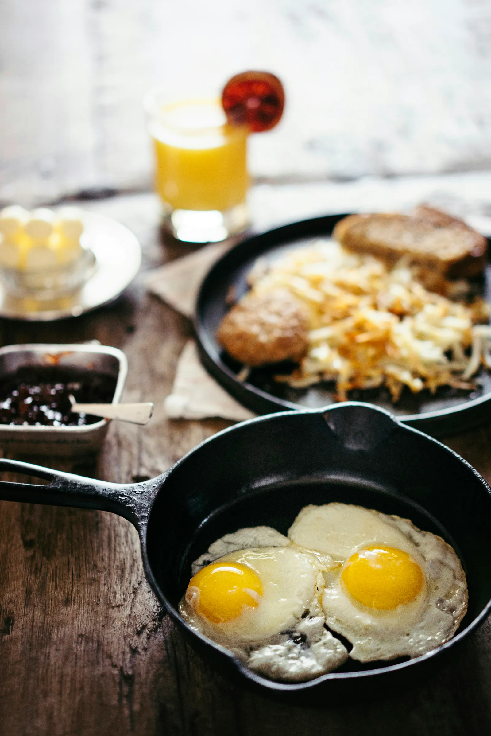 Two sunny-side-up eggs cooked in a cast iron skillet on a wood table, breakfast scene