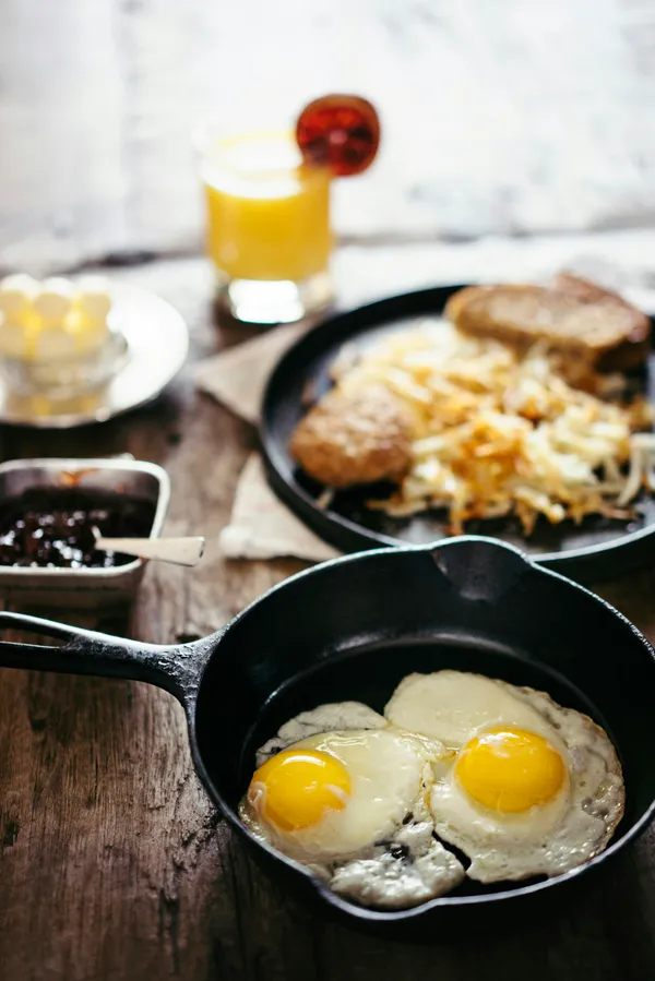 Two sunny-side-up eggs cooked in a cast iron skillet on a wood table, breakfast scene