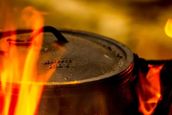 A cast iron dutch oven lid catching flames as the pot braises on coals, dutch oven pot roast in process