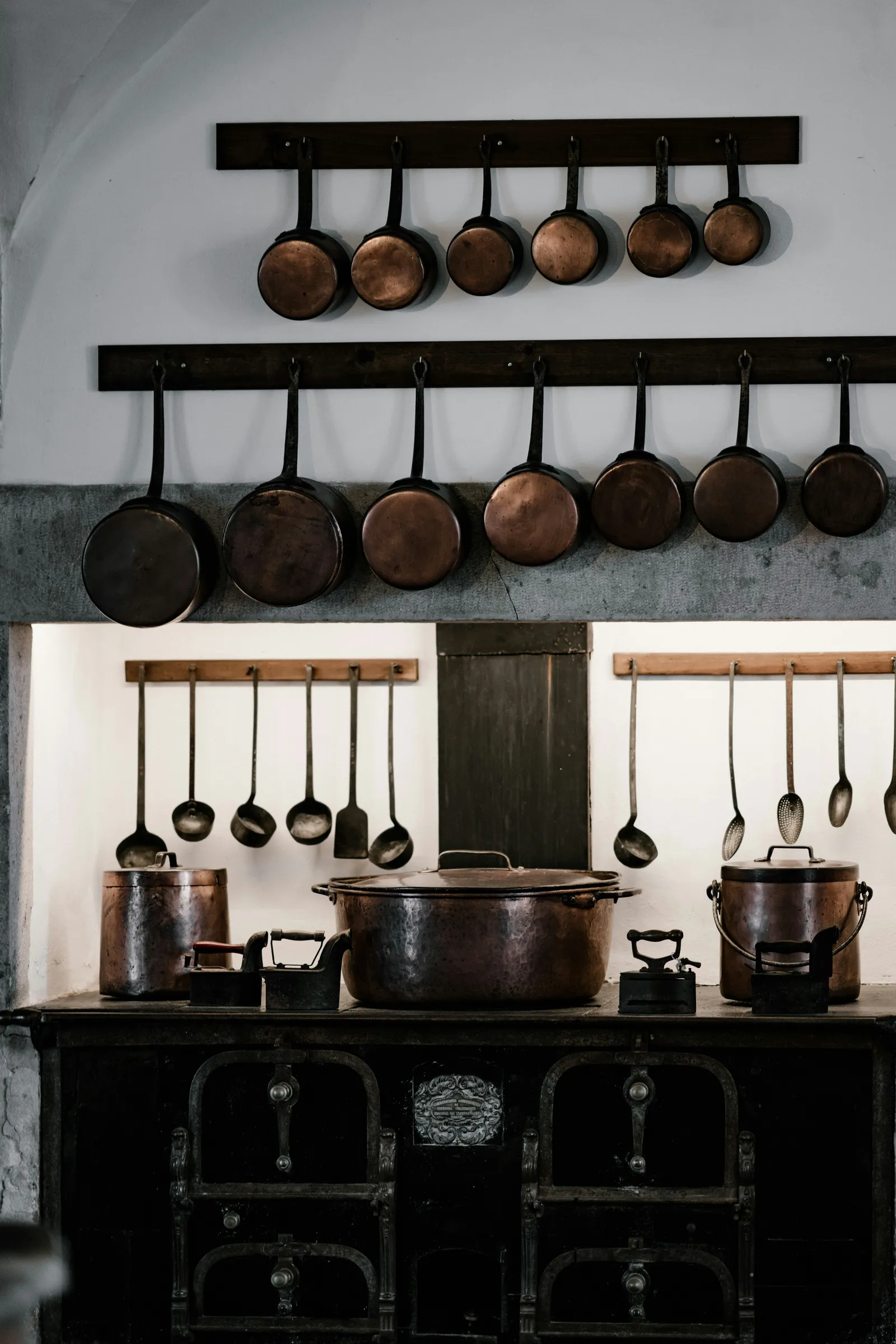 Cast iron and copper cookware hanging on wall rails above a black range, a classic way to store cast iron with good airflow