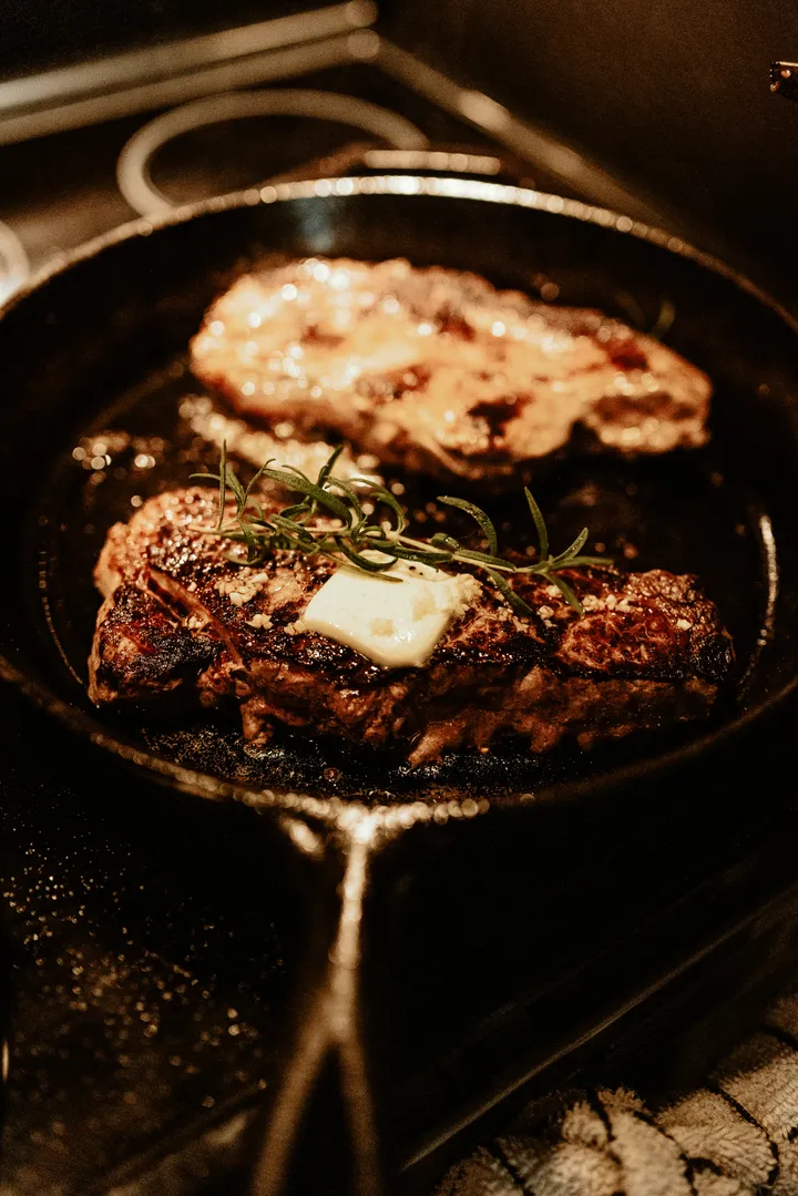 A cast iron skillet searing steaks on an electric stovetop, the heavy pan glass-top stove owners ask about