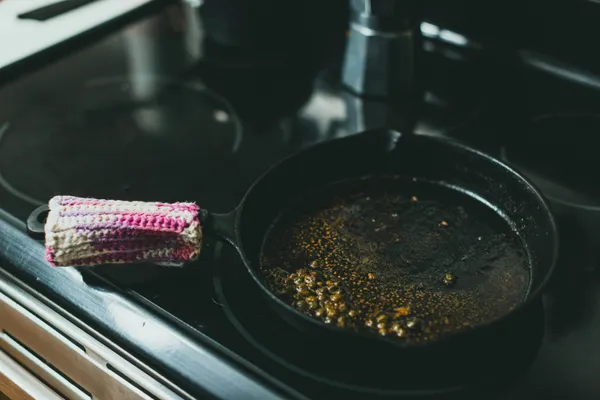 A cast iron skillet on a stovetop with residue from a previous cook, the kind of pan that needs re-seasoning