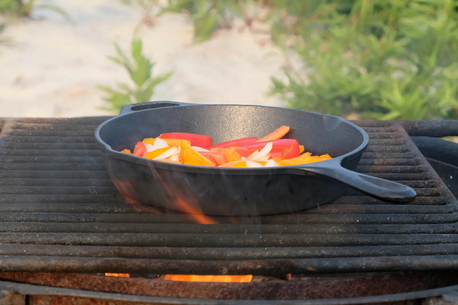 A black cast iron skillet cooking peppers and onions, its dark seasoned surface visible