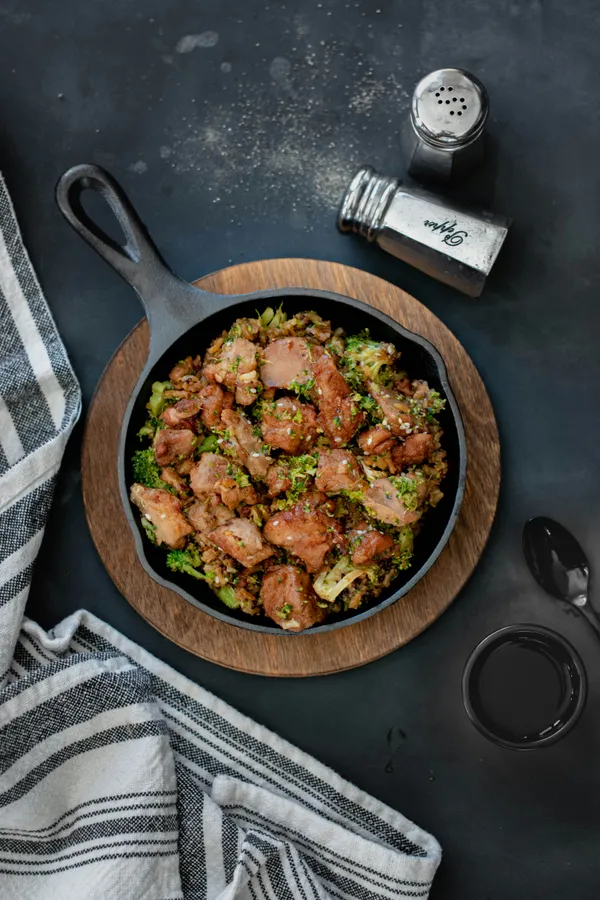Browned chicken and broccoli cooked in a black cast iron skillet on a dark surface
