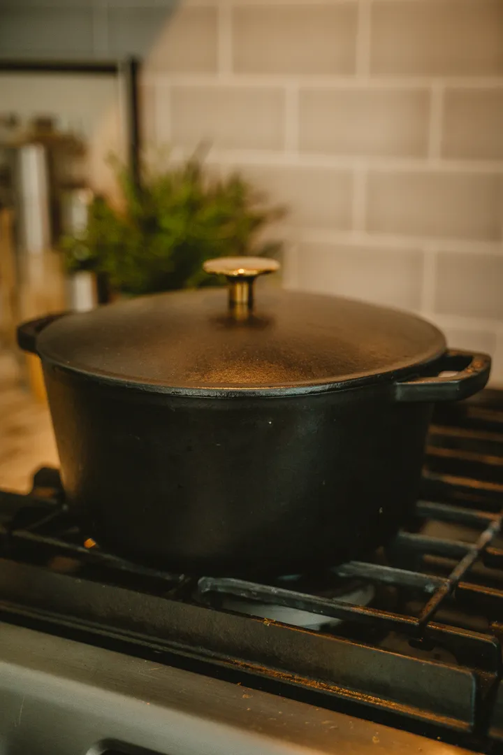 A seasoned bare cast iron Dutch oven with lid on a gas stovetop, ready to season