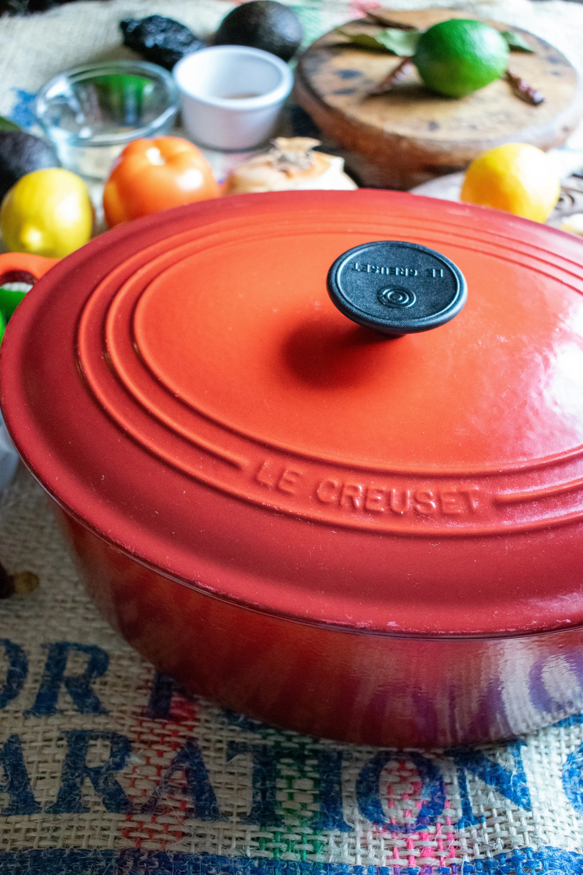 A red Le Creuset enameled cast iron dutch oven with the lid on, surrounded by fresh produce