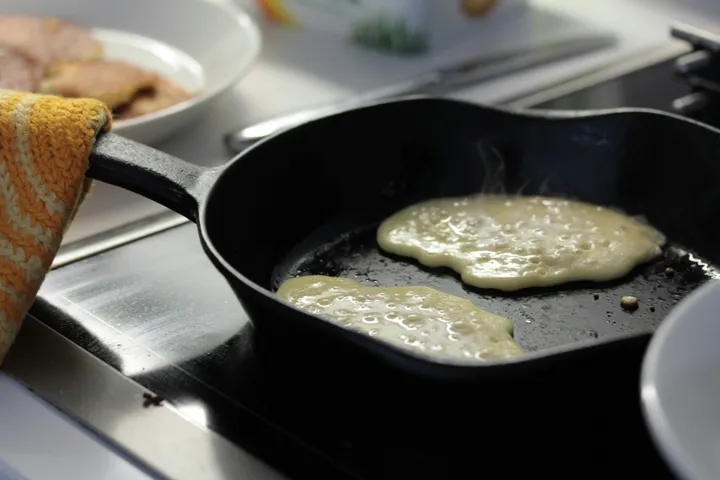 Pancakes cooking in a cast iron skillet with bubbles forming across the batter