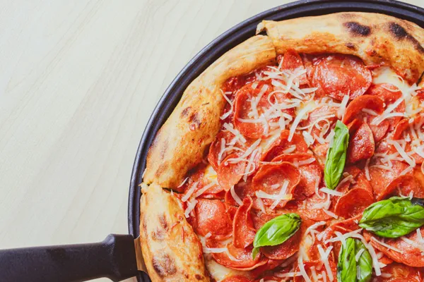 A pepperoni cast iron skillet pizza with puffy crust, melted parmesan, and basil